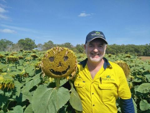 Man standing in field of sunflowers one flower has a smiley face